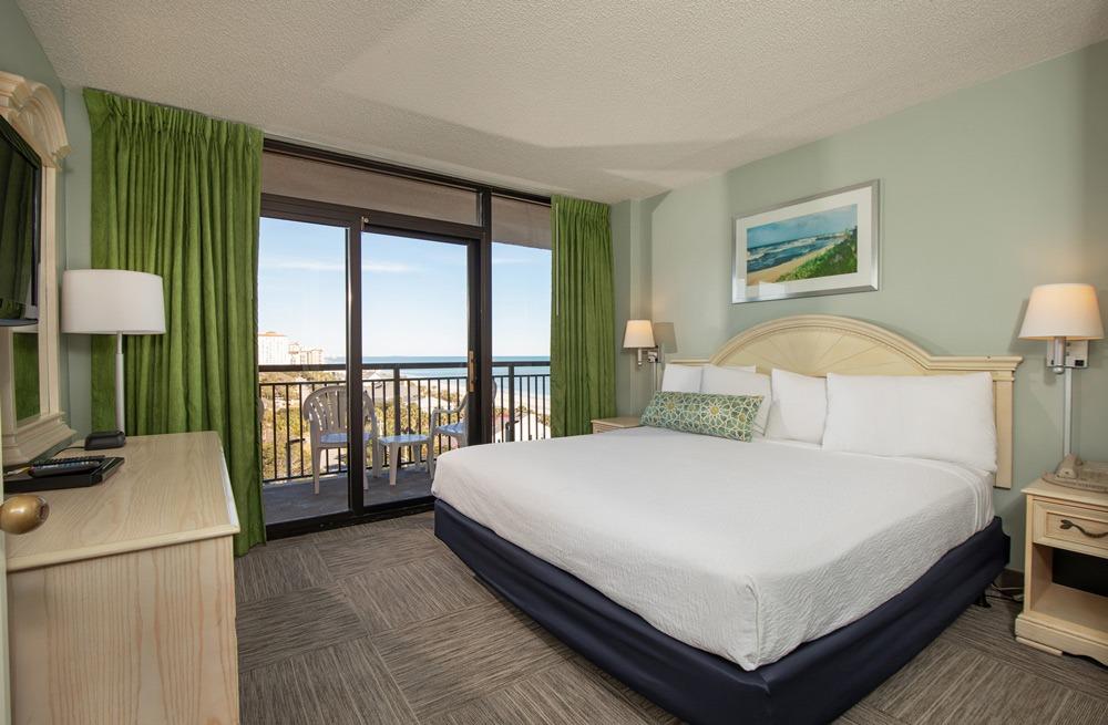 The spacious and inviting bedroom in a three-bedroom ocean-view condo at Grande Shores Ocean Resort features a comfortable king-sized bed, modern decor, and a private balcony overlooking the ocean.