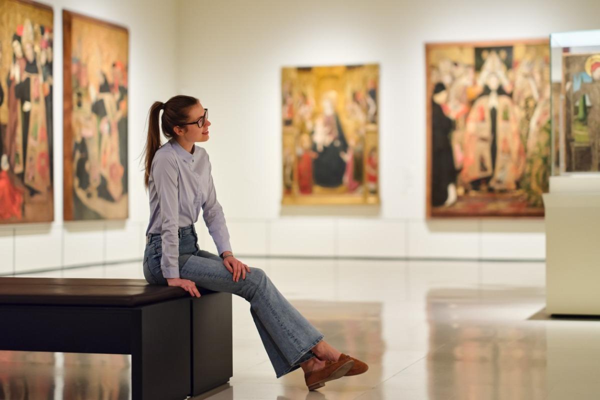 Thoughtful young Caucasian woman wearing glasses and looking at exhibition.