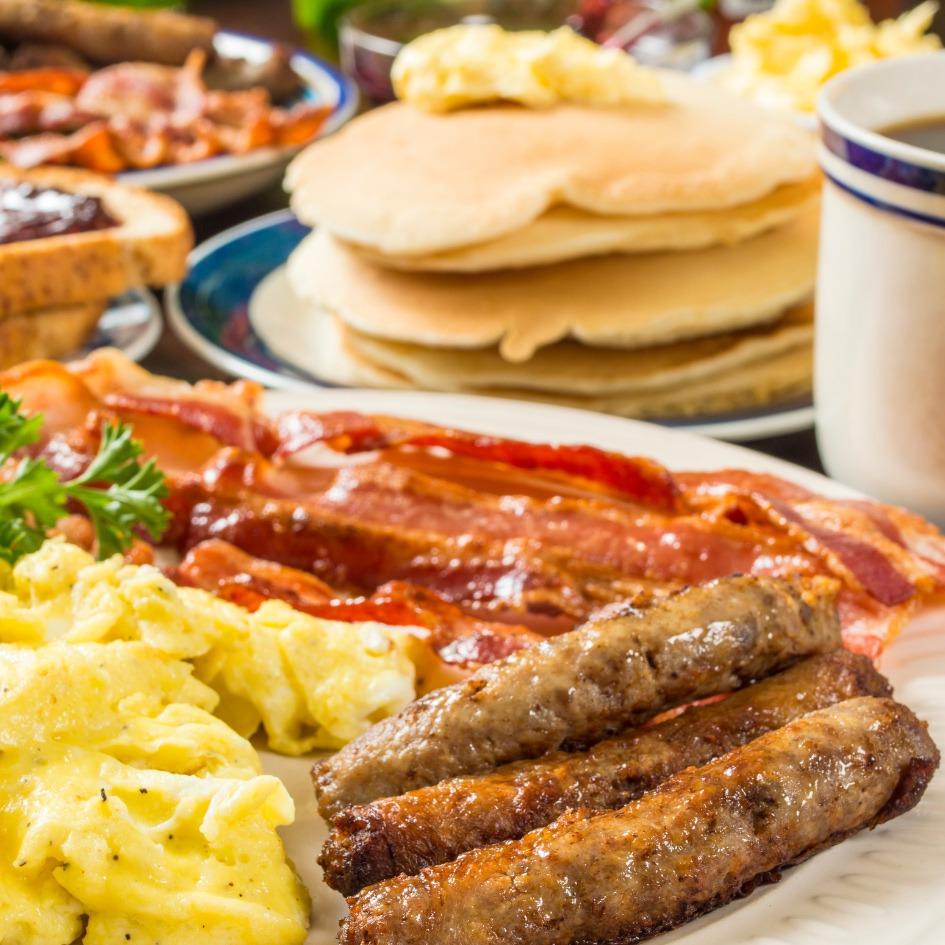 Assortment of breakfast items including sausage links, scrambled eggs, bacon, toast with jelly, and pancakes.