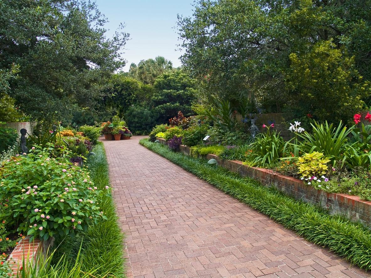 a brick pathway at brookgreen gardens with lush greenery and statues