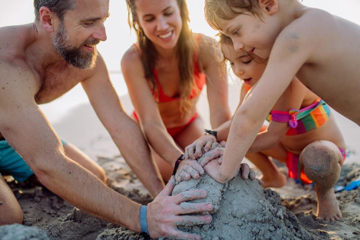 Happy family with little kids enjoying time at the beach building a sandcastle.