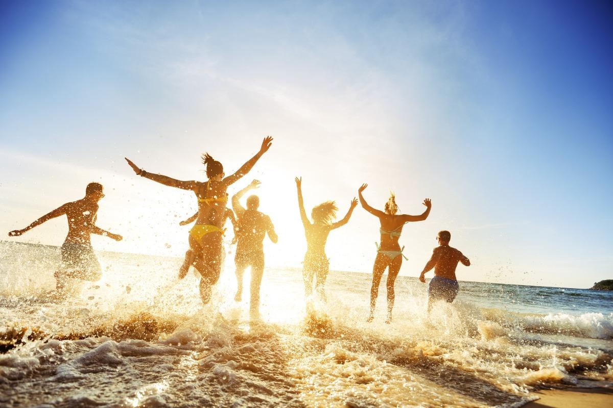 A group of happy beachgoers in swimwear joyfully jumping and splashing in the ocean waves under a bright sun, showcasing the fun, energetic atmosphere of a family friendly Myrtle Beach getaway.