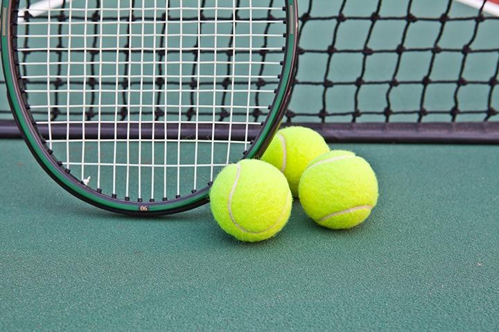 Three tennis balls next to a racket on a tennis pitch