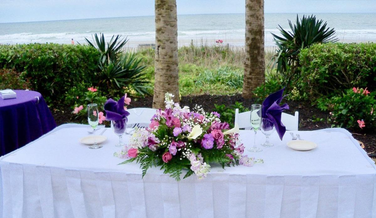 Elegant outdoor wedding table setting with a floral centerpiece by the beach.