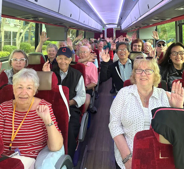 Smiling group of people with their hands up in the air inside a motorcoach tour bus