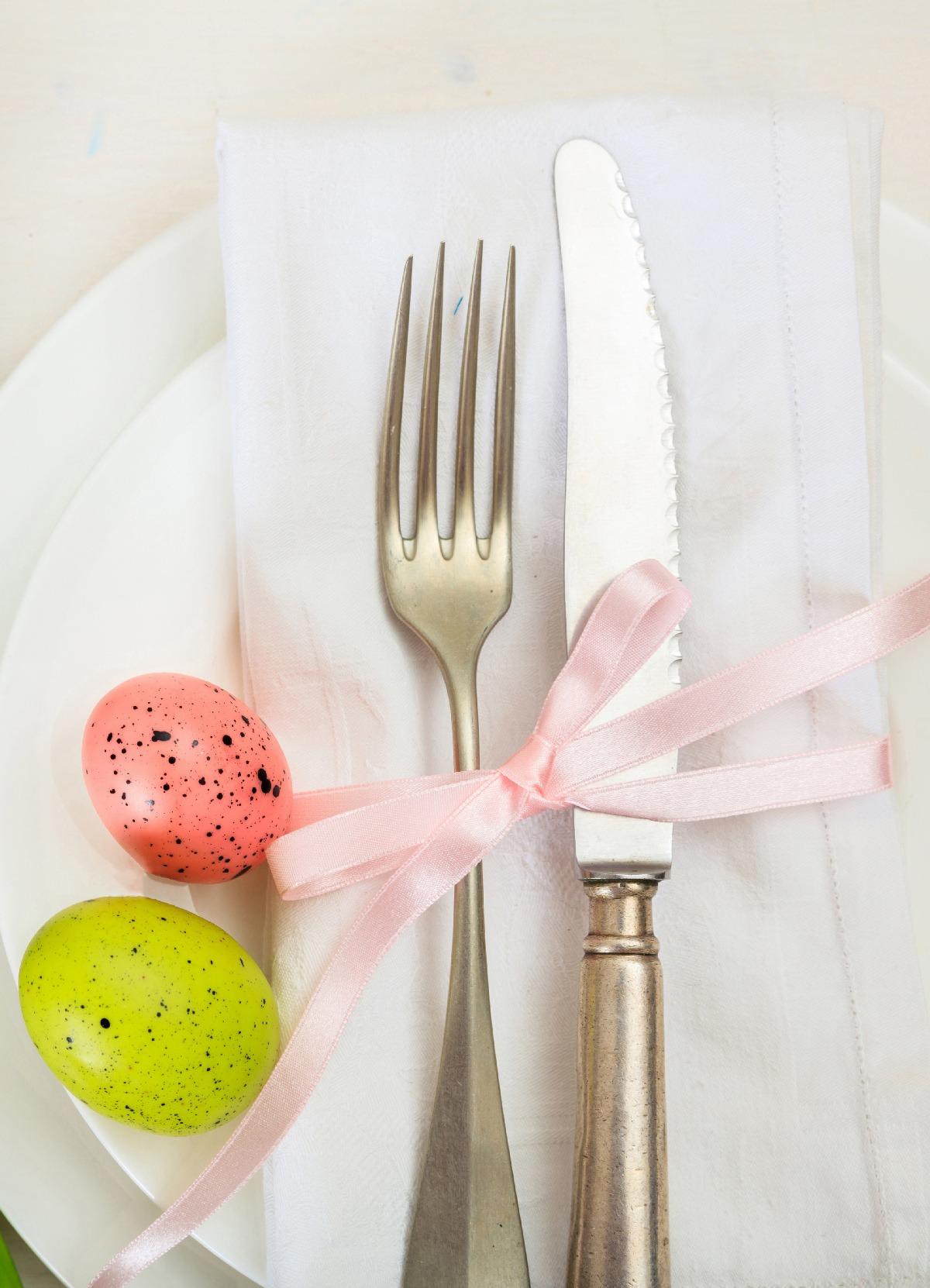 Elegant table setting with cutlery, napkin, ribbon, and colorful Easter eggs.