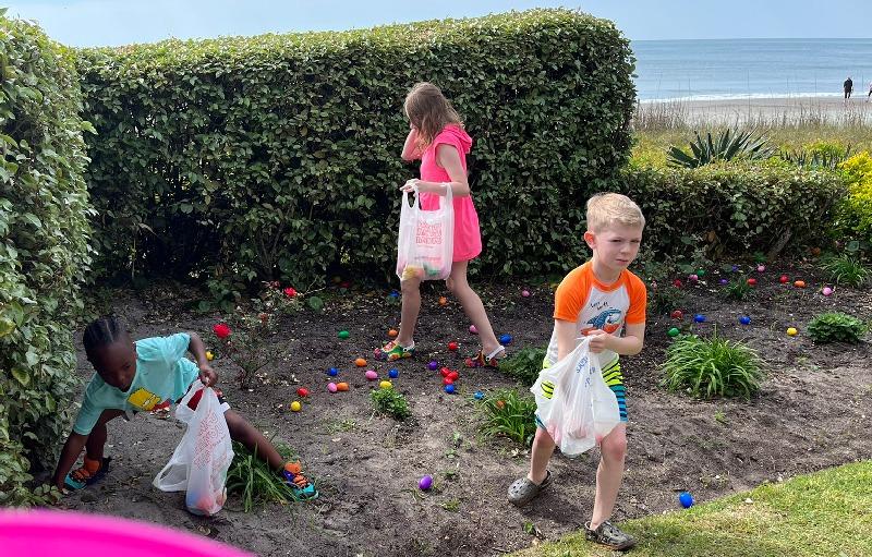 Children collecting colorful Easter eggs in a garden by the beach.