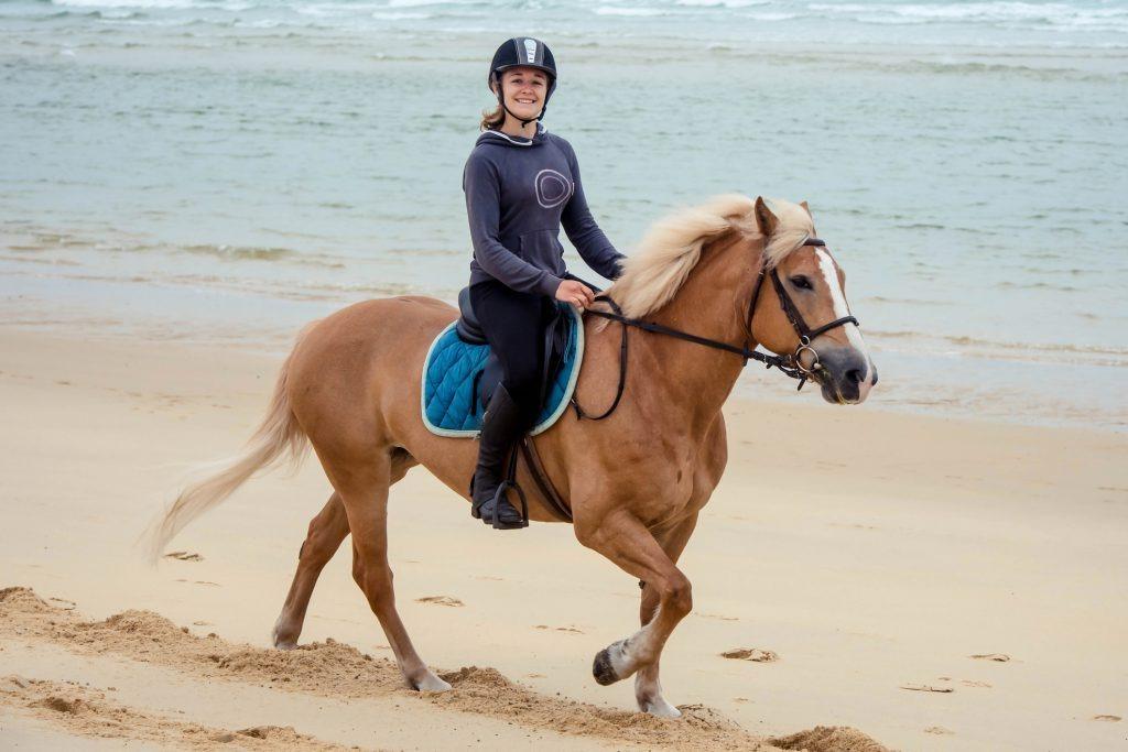 a young girl riding a horse on the sand by the ocean