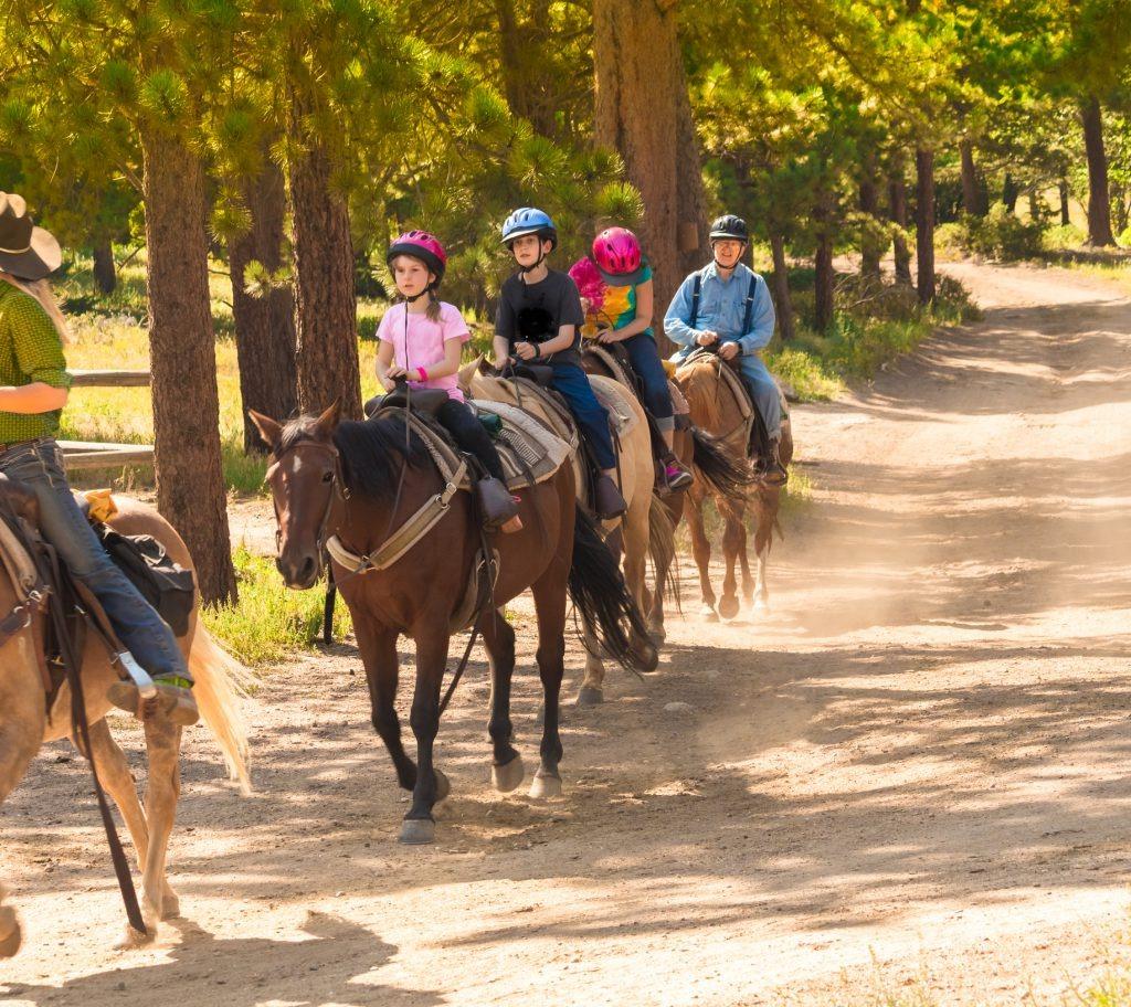 Several kids and an adult riding on horses on a trail ride