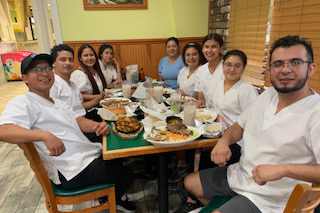 Group of smiling people in white shirts dining together at a restaurant.