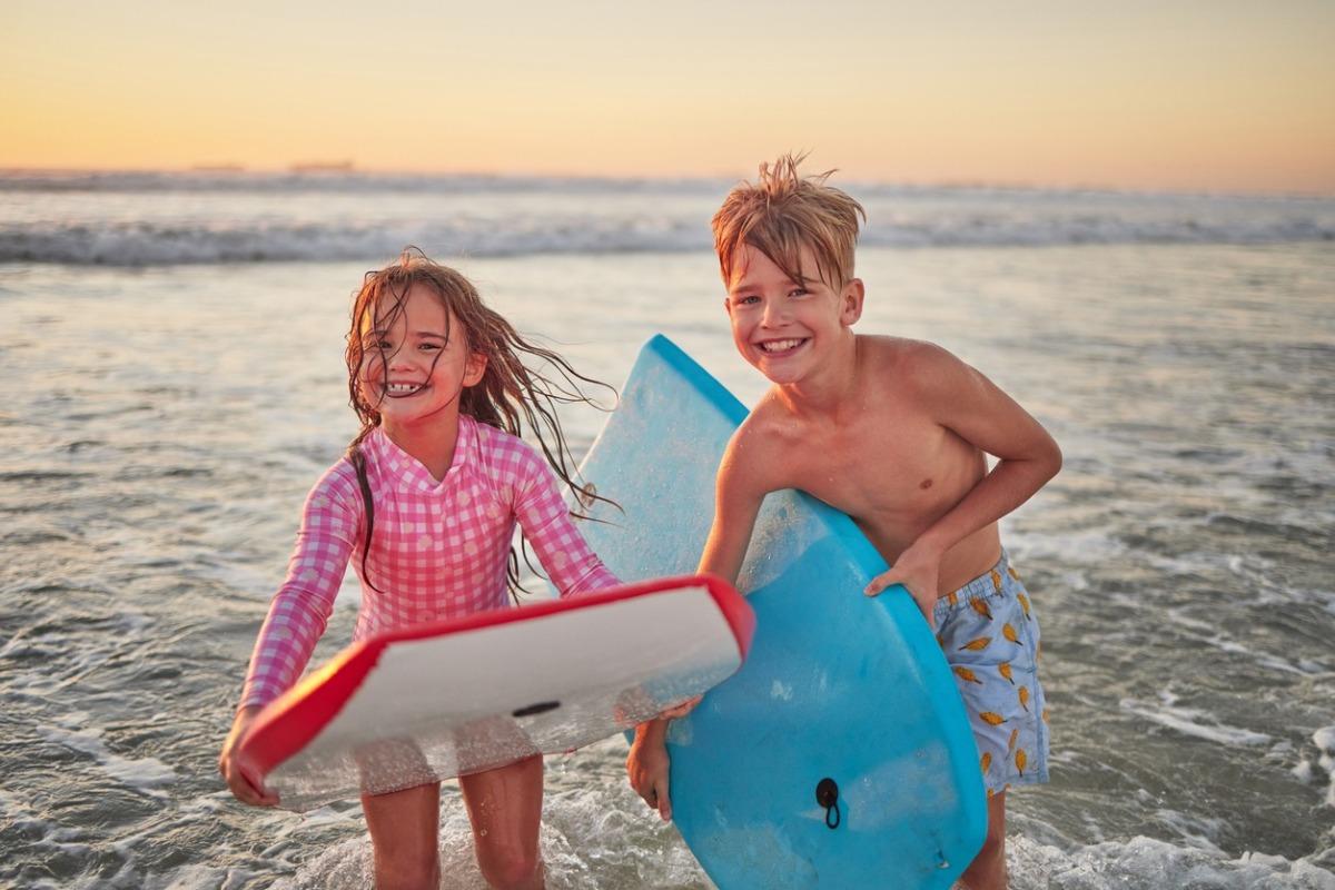 Happy children, beach and learning to surf for fun and bonding on bali summer vacation.