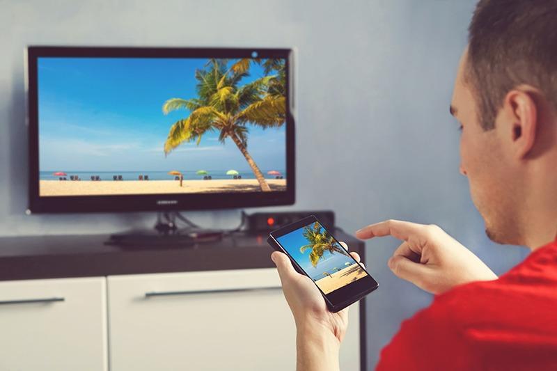 Person holding a mobile phone casting the image to a flat screen TV in the background