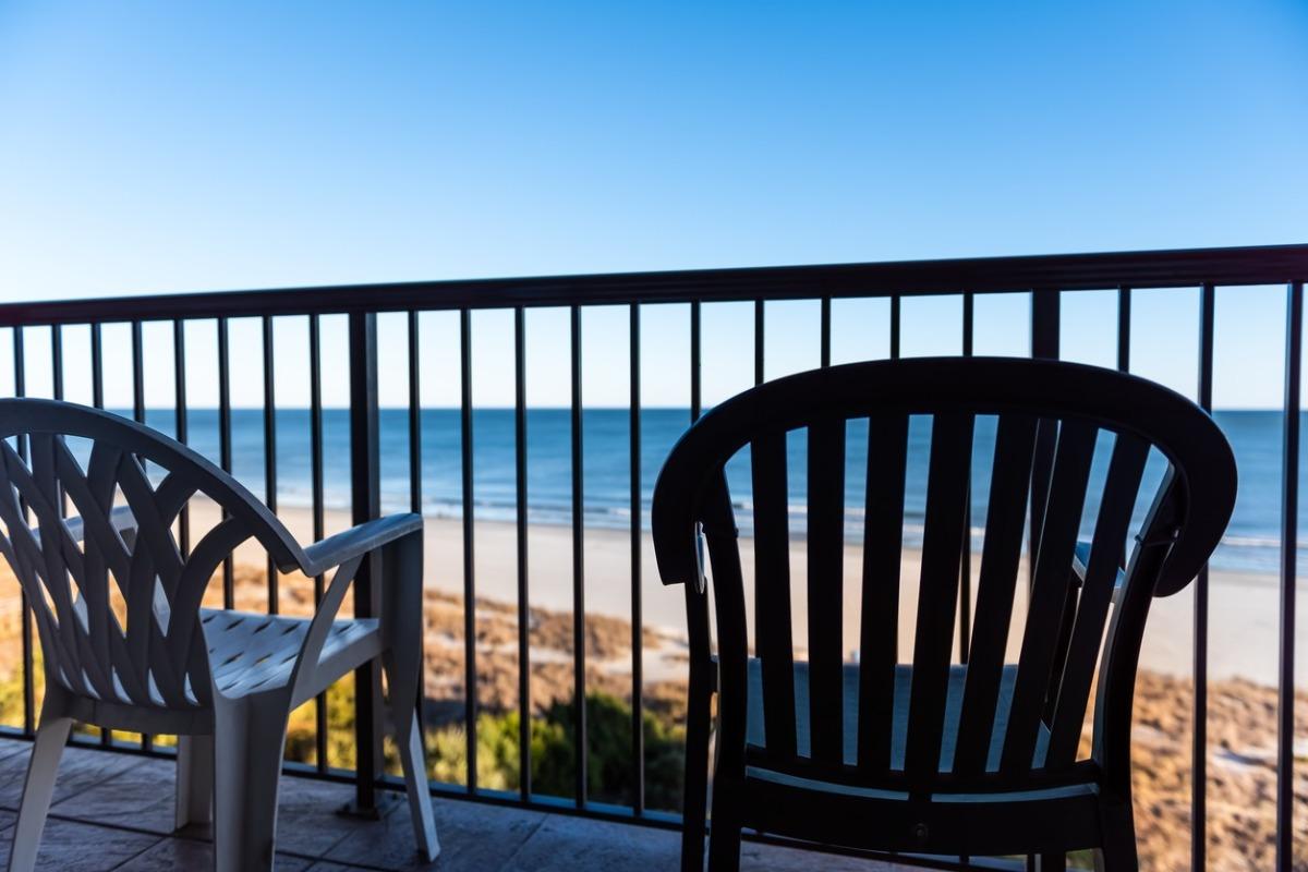 Oceanfront balcony view at Grande Shores Ocean Resort with two chairs overlooking the sandy Myrtle Beach shoreline under a clear blue sky.