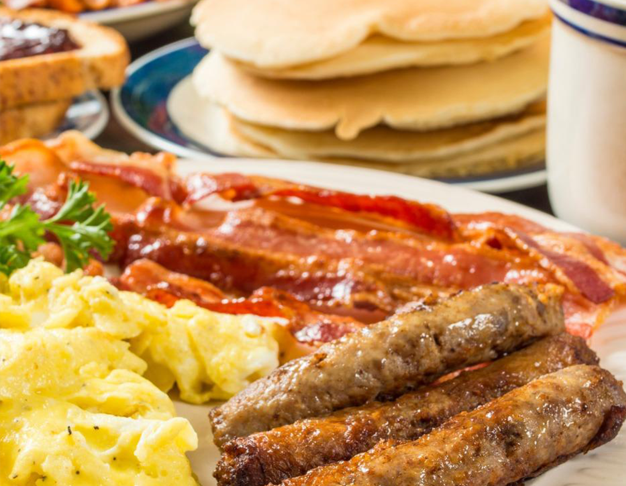 Plate with breakfast items including scrambled eggs, sausage links, bacon, pancakes and toast & jelly.