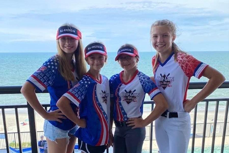 Four young athletes, three girls and one boy, are standing on a balcony with a view of the ocean in the background.