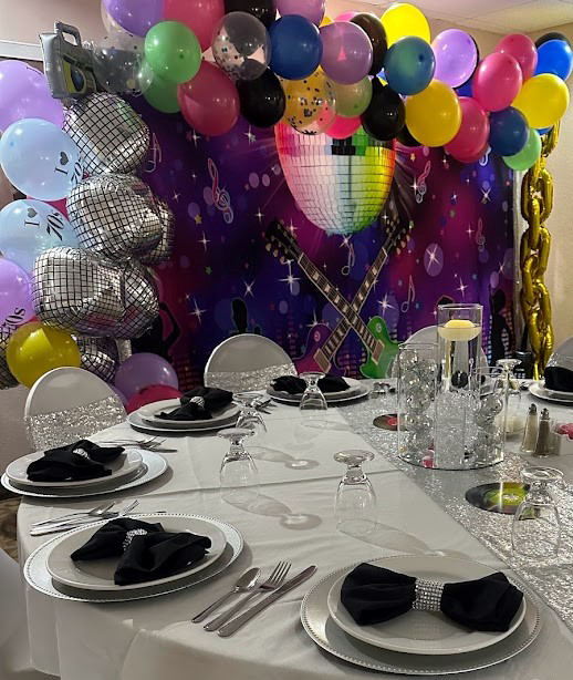 Festive party table setting with colorful balloons and music-themed backdrop.