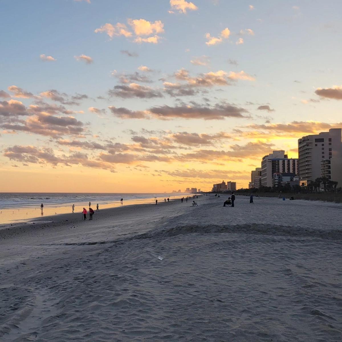 photo of the sunset on the beach in front of Grande Shores Resort with the sand and waters along with people walking on the shoreline